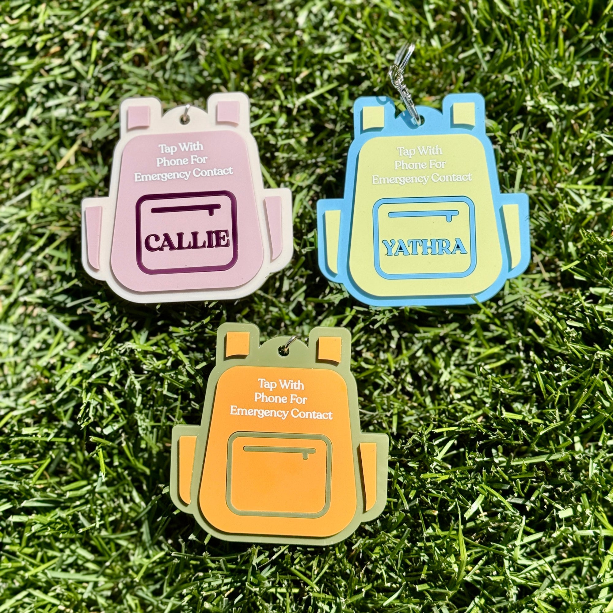Three backpack-shaped keychains on grass