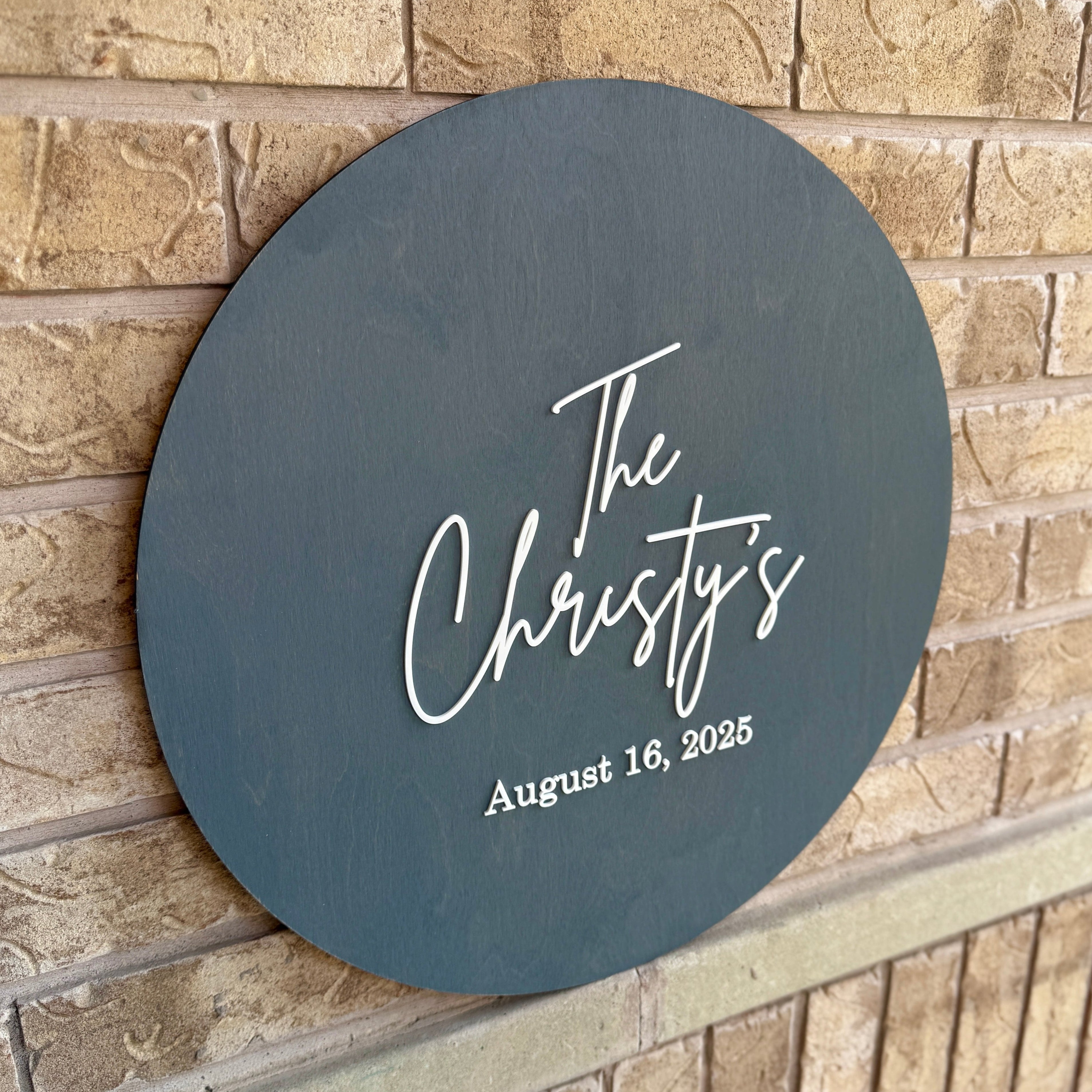 Round dark gray sign with 'The Christy's' and date on a brick wall