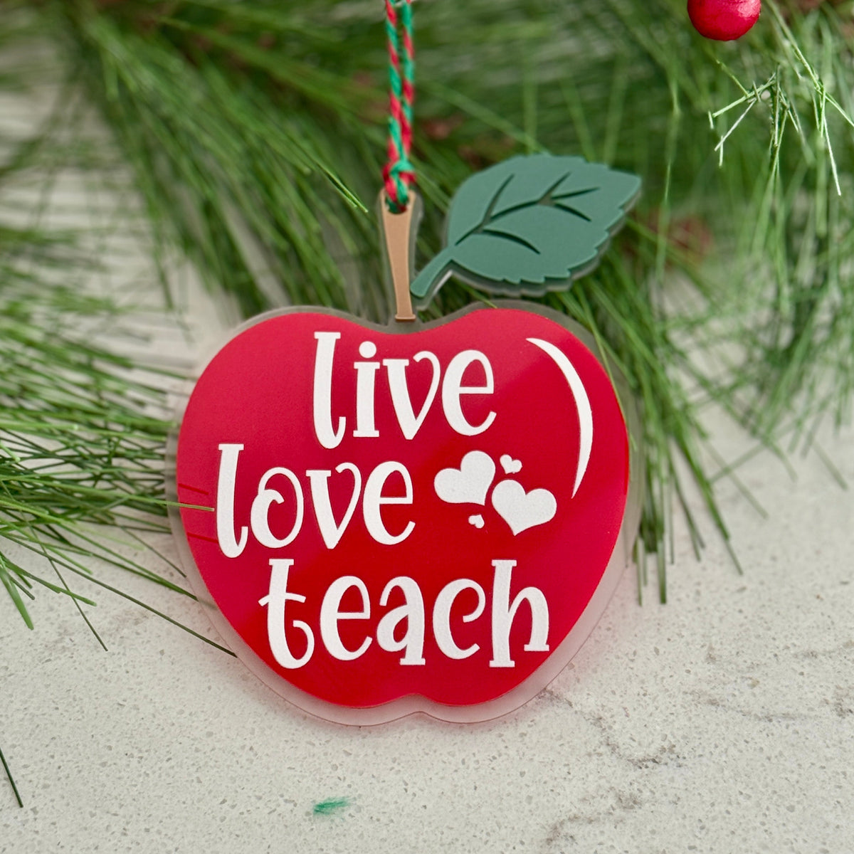Decorative ornament shaped like a red apple with 'Live Love Teach' text, hanging on a Christmas tree.