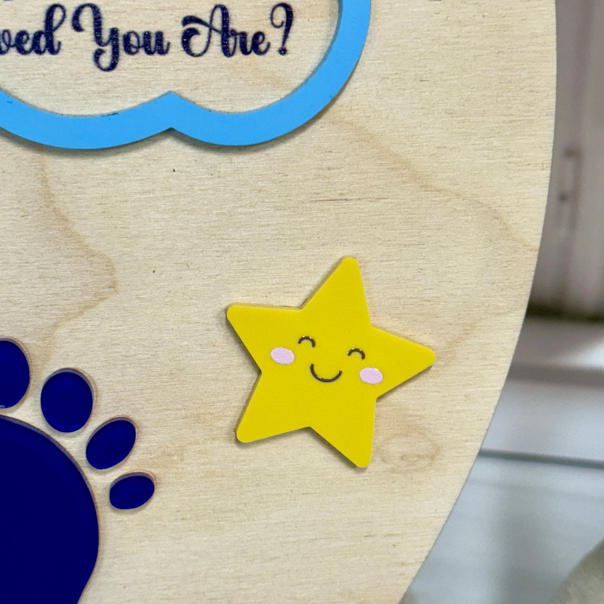 Wooden plaque with a yellow star, blue paw print, and question mark on a light wood background.