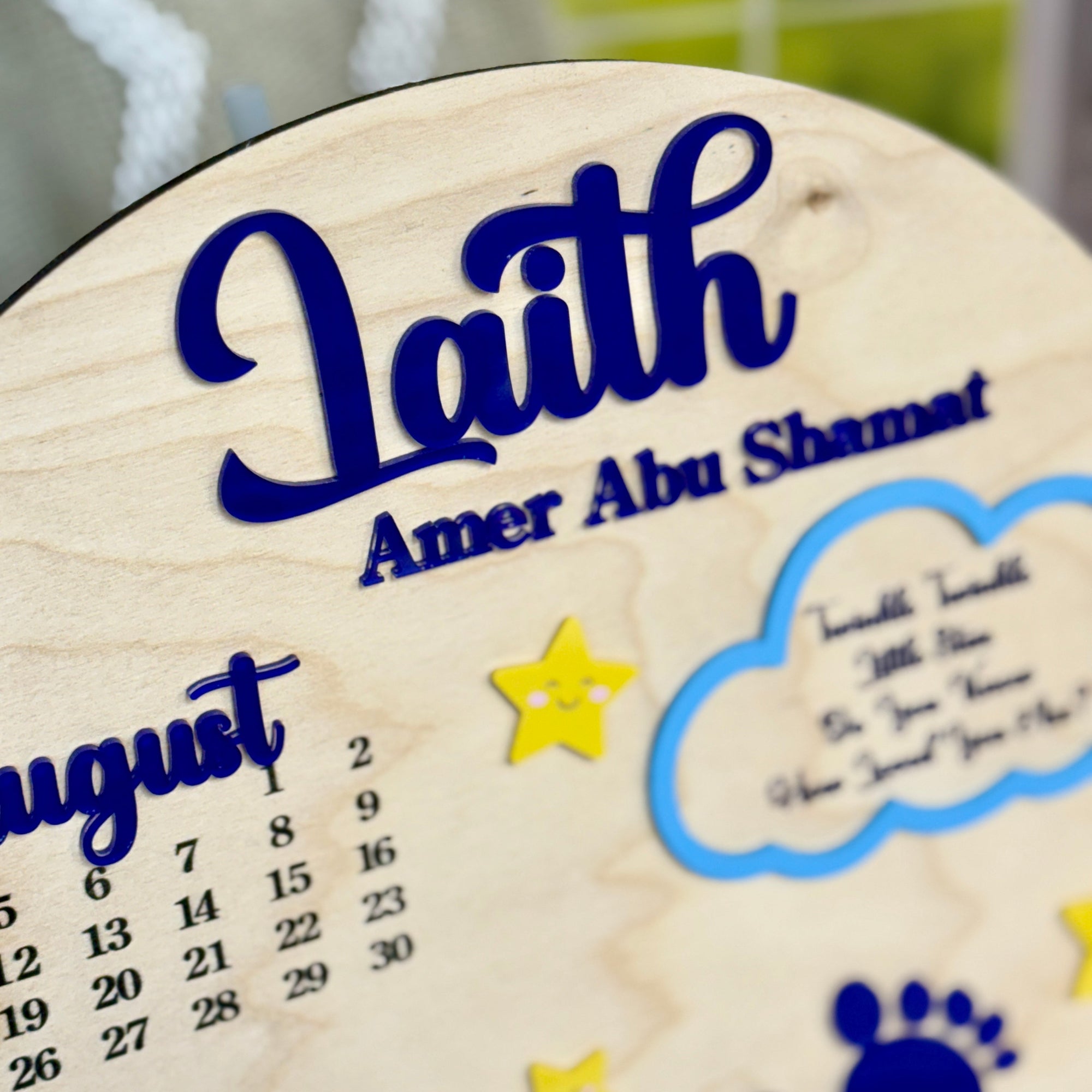 Wooden circular plaque with engraved name 'Laith' and calendar, featuring stars and footprints.
