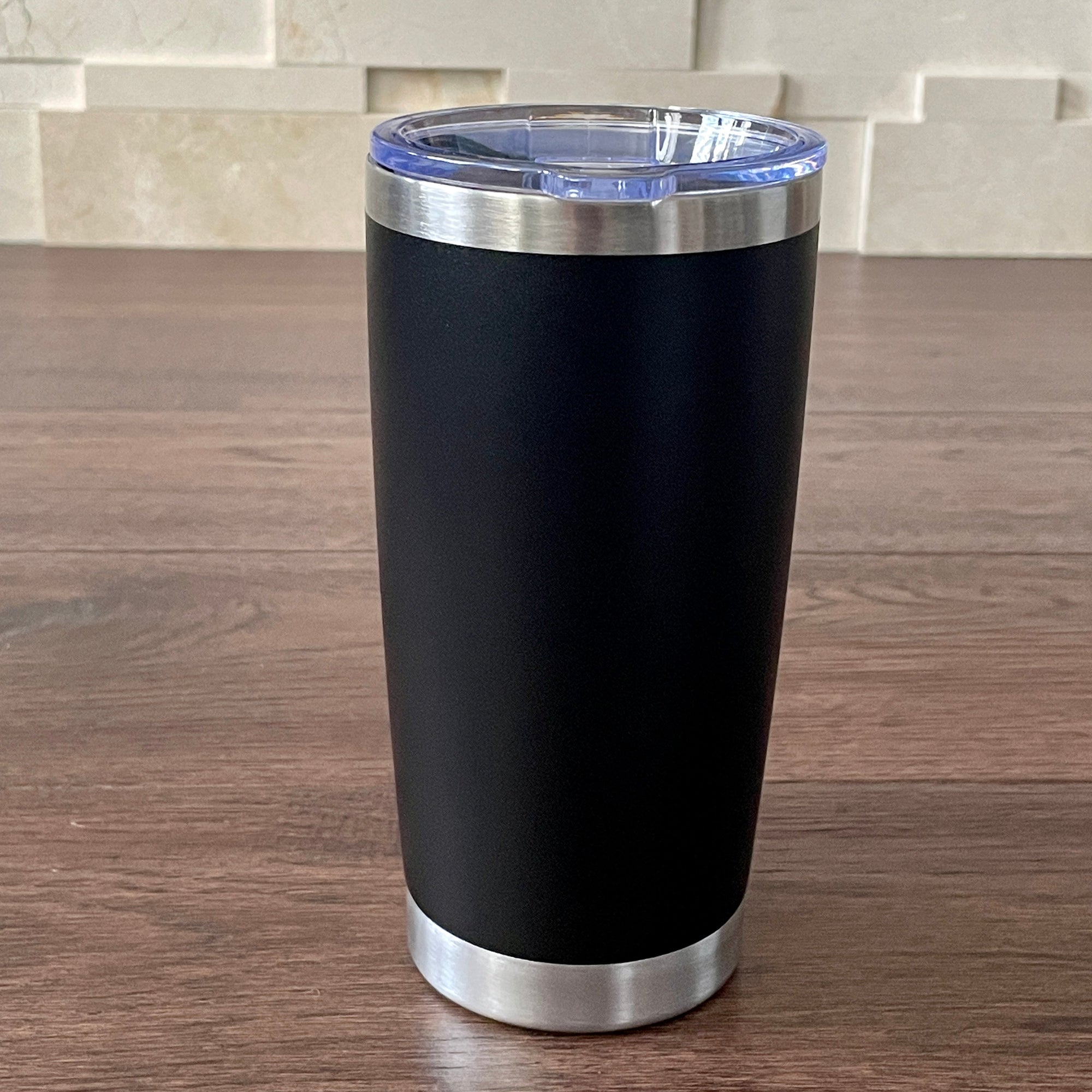 Black insulated tumbler with silver base and lid on a wooden surface.
