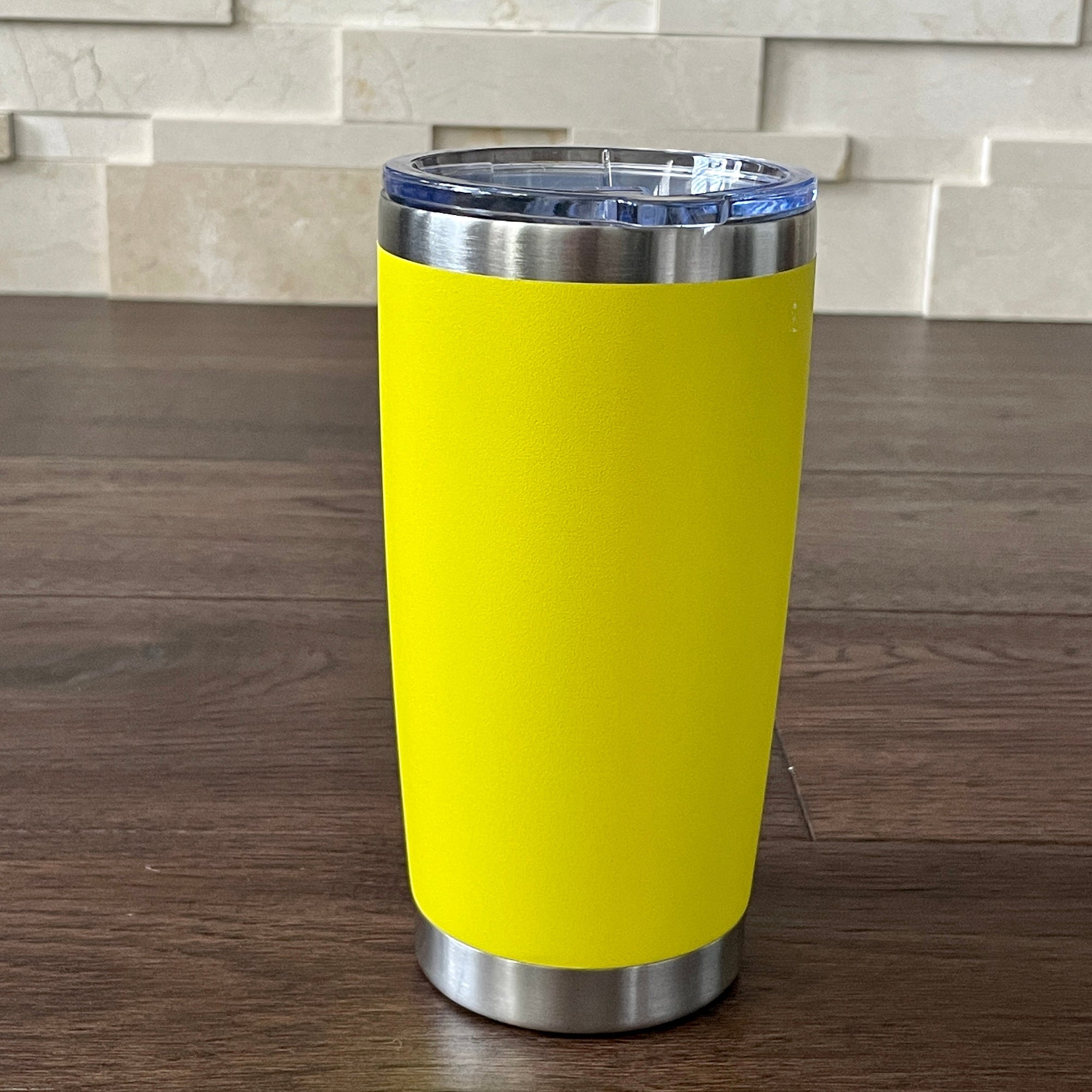 Yellow tumbler with a silver base and lid on a wooden surface with a stone wall background