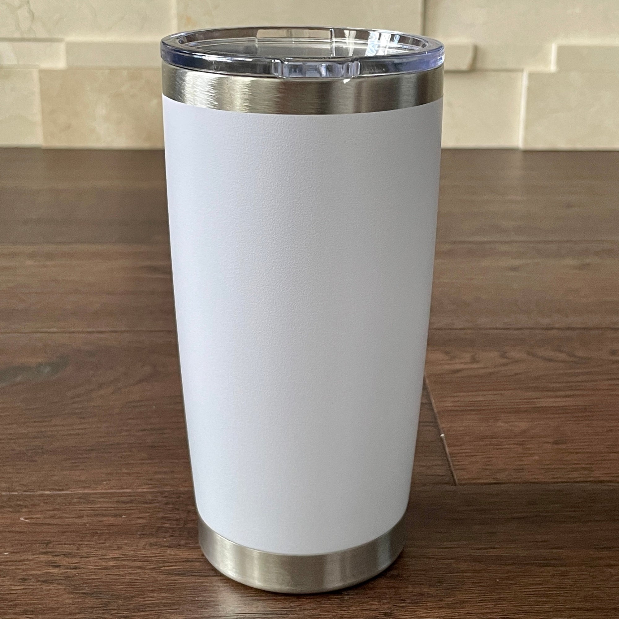 White tumbler with silver base and lid on a wooden surface.