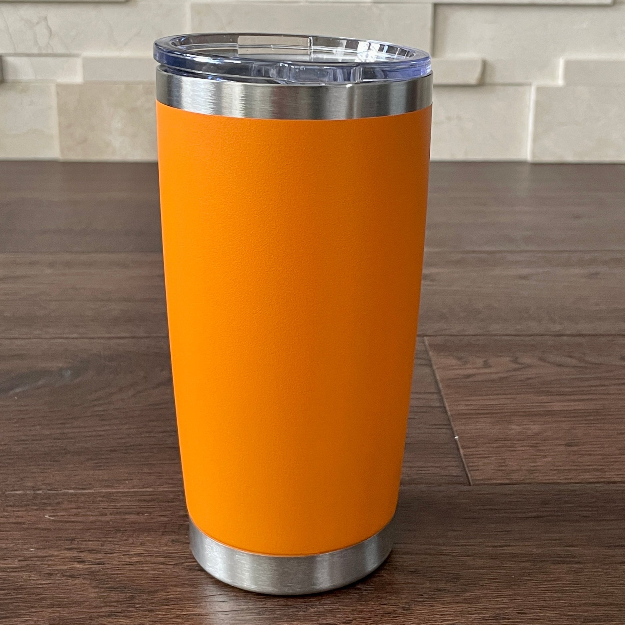 Orange tumbler with a silver base and lid on a wooden surface.