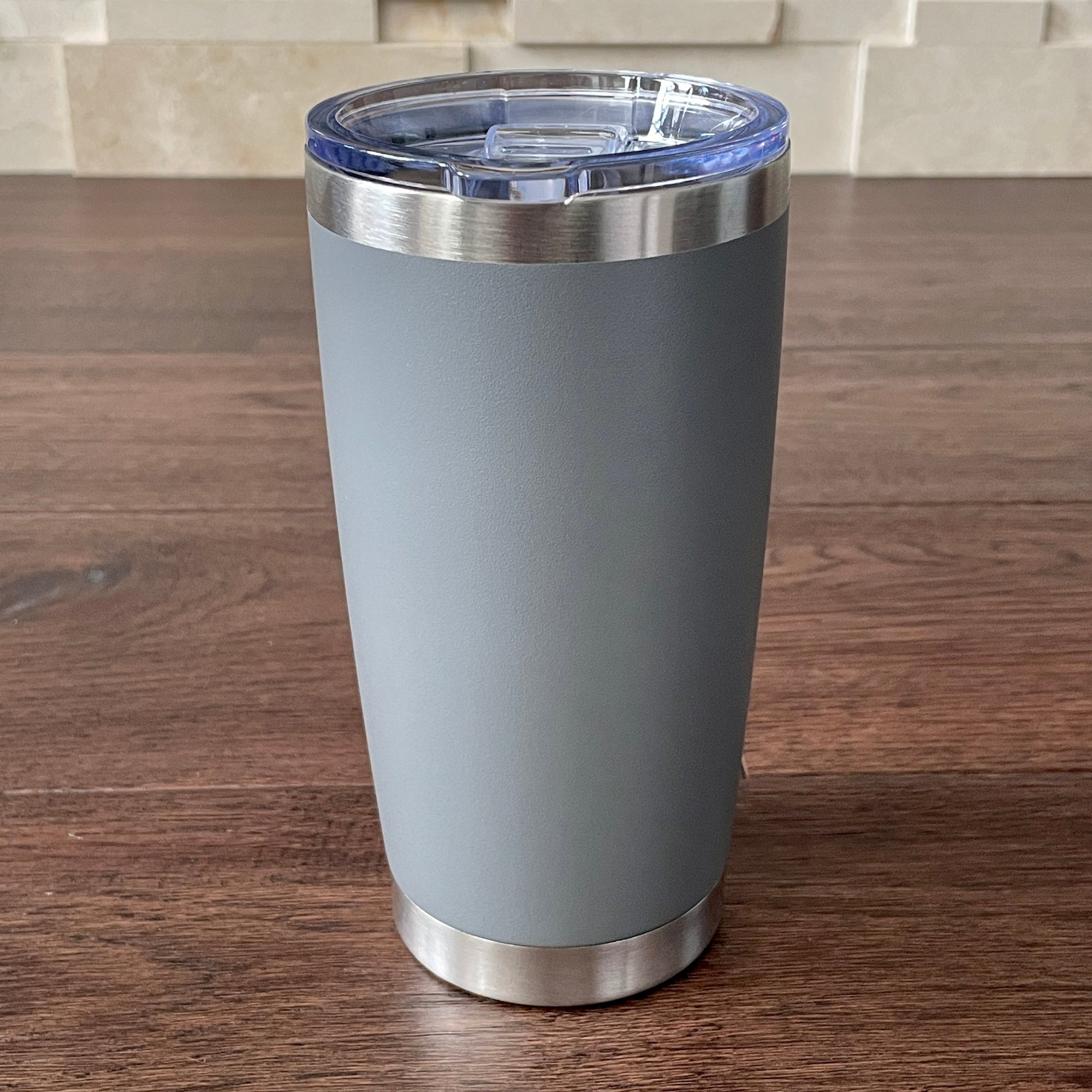 Gray tumbler with a silver base and lid on a wooden surface.