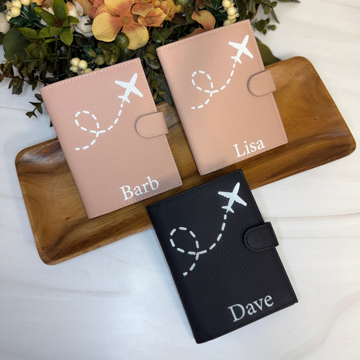 Three personalized passport holders on a wooden tray with flowers in the background