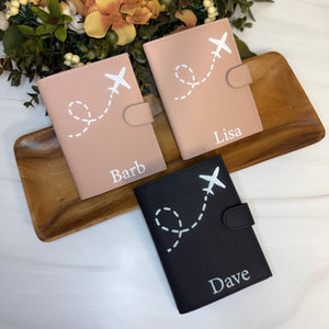 Three personalized passport holders on a wooden tray with flowers in the background