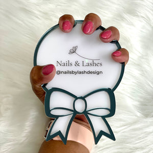 Hand holding a round mirror with 'Nails & Lashes' branding on a white fluffy background
