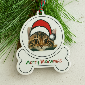 American Shorthair Cat ornament with Santa hat and 'Merry Meowmas' text on a white surface with greenery.