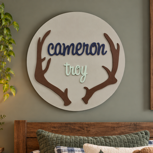 Personalized round wooden deer antler nursery name sign featuring raised name.