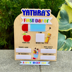 Wooden first day of school sign with colorful text and graphics on a stone surface.