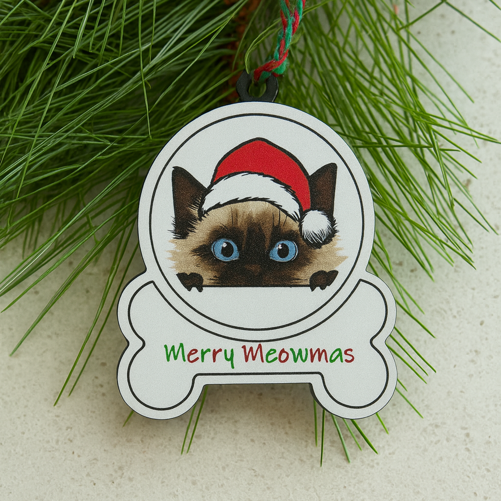 Balinese Cat ornament with Santa hat and 'Merry Meowmas' text on a white surface with greenery.
