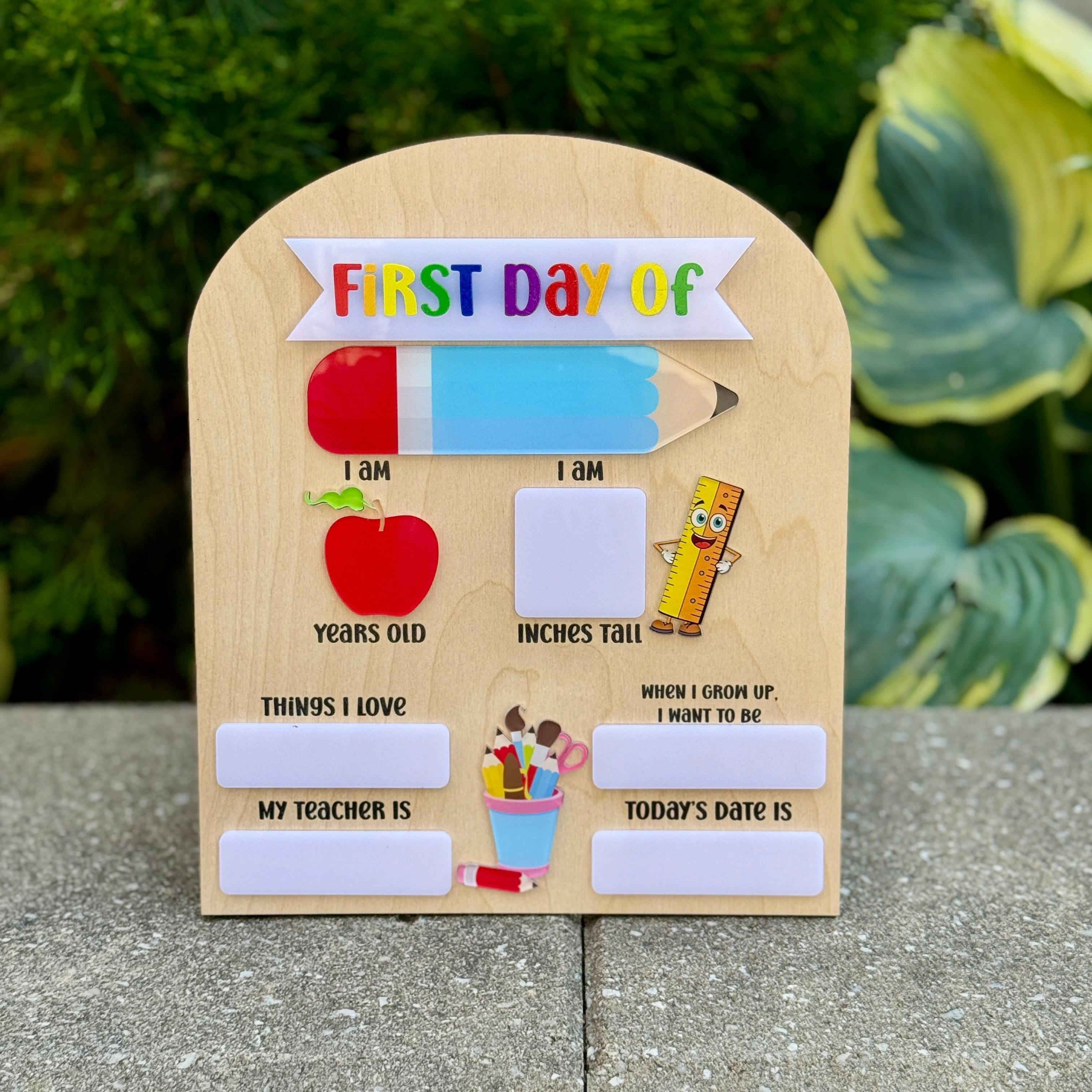 Wooden sign for the 'First Day of School' with various sections to fill out, placed outdoors.