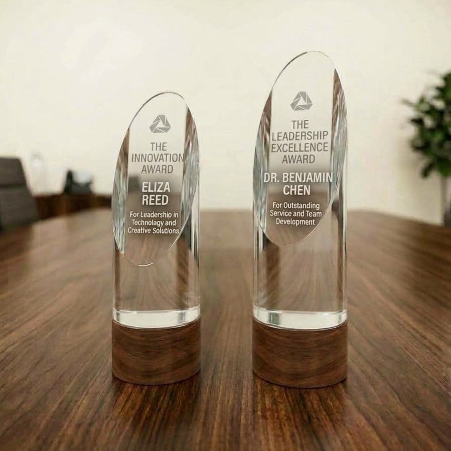 Two clear acrylic award trophies with wooden bases standing on a dark wood table in an indoor setting.