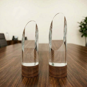 Clear crystal oval arch corporate award with a dark wood-finish base displayed on a wooden tabletop.