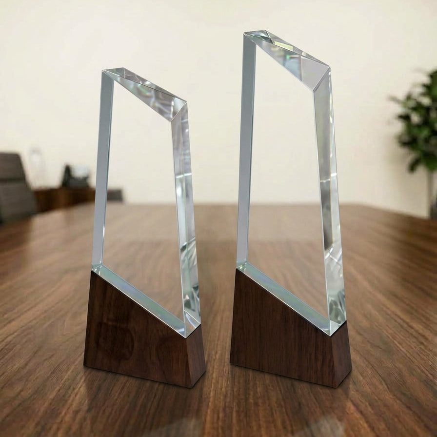 Two tall geometric crystal awards with slanted tops and angled dark walnut wood bases on a conference table.