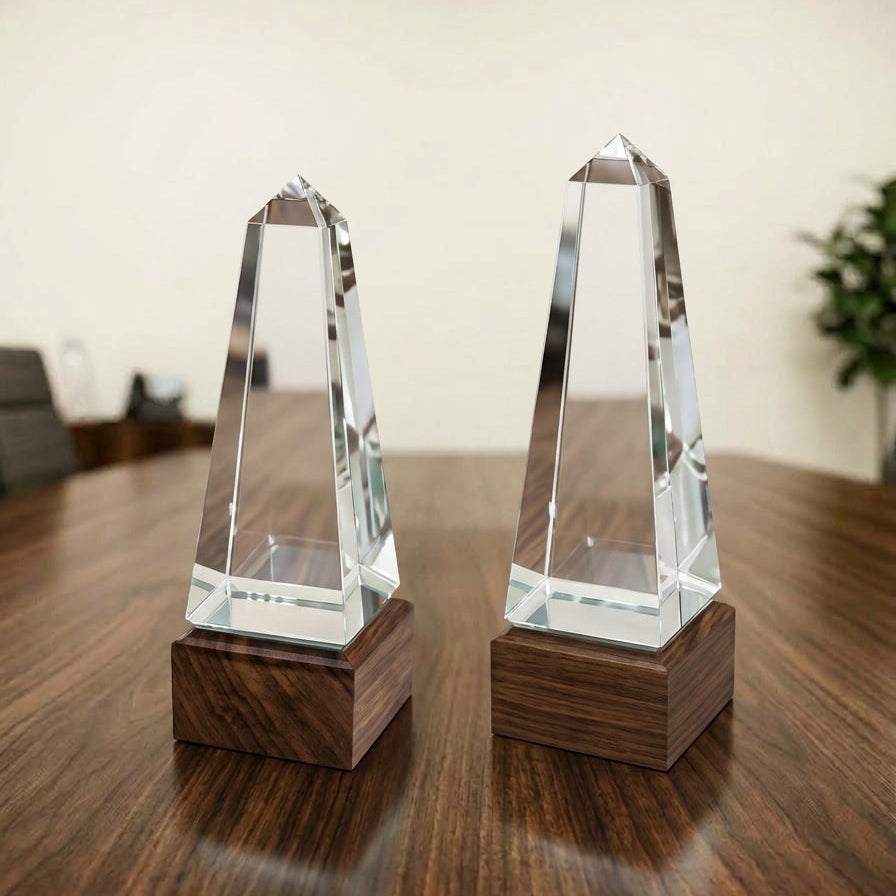 Premium clear crystal obelisk corporate award with a dark wood-finish base displayed on a wooden table.
