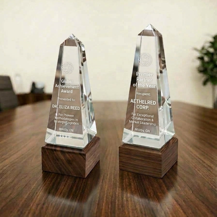 Two clear crystal award plaques with engraved text, mounted on dark wooden bases, displayed on a polished wooden table in an indoor setting.