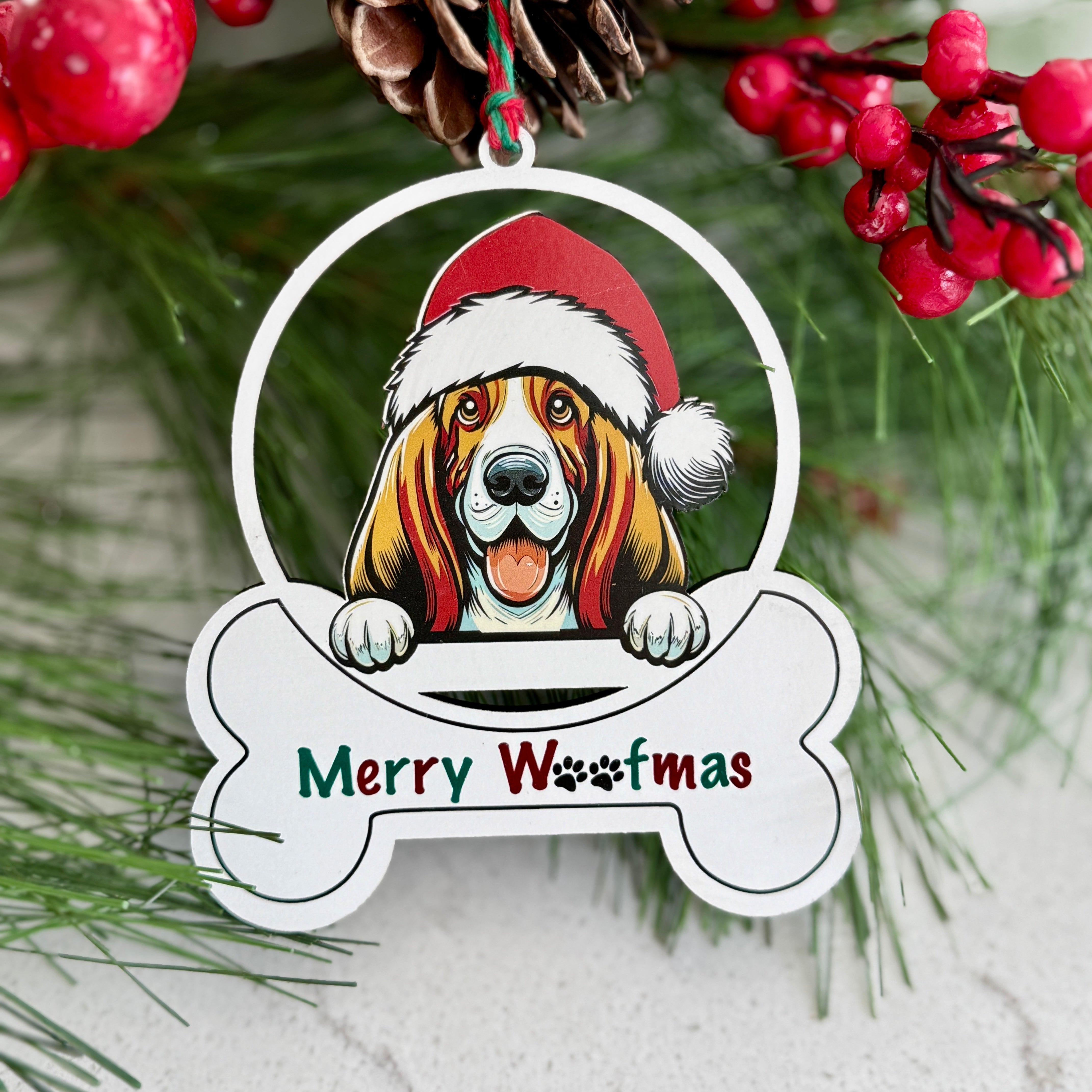 Christmas ornament with a dog wearing a Santa hat and 'Merry Woofmas' text, surrounded by greenery and berries.