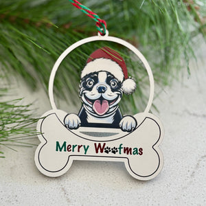 Christmas ornament with a dog wearing a Santa hat and 'Merry Woofmas' text, hanging on a pine branch.