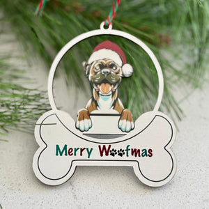 Christmas ornament with a dog wearing a Santa hat and 'Merry Woofmas' text, surrounded by pine branches and berries.