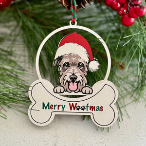 Christmas ornament with a dog wearing a Santa hat and 'Merry Woofmas' text, surrounded by pine branches and berries.