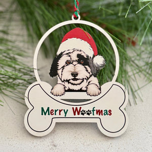 Christmas ornament with a dog wearing a Santa hat and 'Merry Woofmas' text, surrounded by pine branches and red berries.