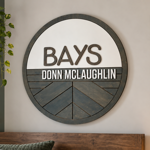 Personalized round wooden nursery name sign featuring names  in raised 3D lettering, neutral wood tones and engraved geometric chevron pattern.