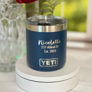 Blue YETI mug with engraved text on a white surface with flowers in the background