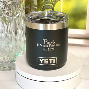 Black YETI mug with silver interior on a white surface next to pink flowers in a glass vase.