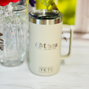 Cream-colored mug with 'YETI' logo on a white surface with flowers in the background