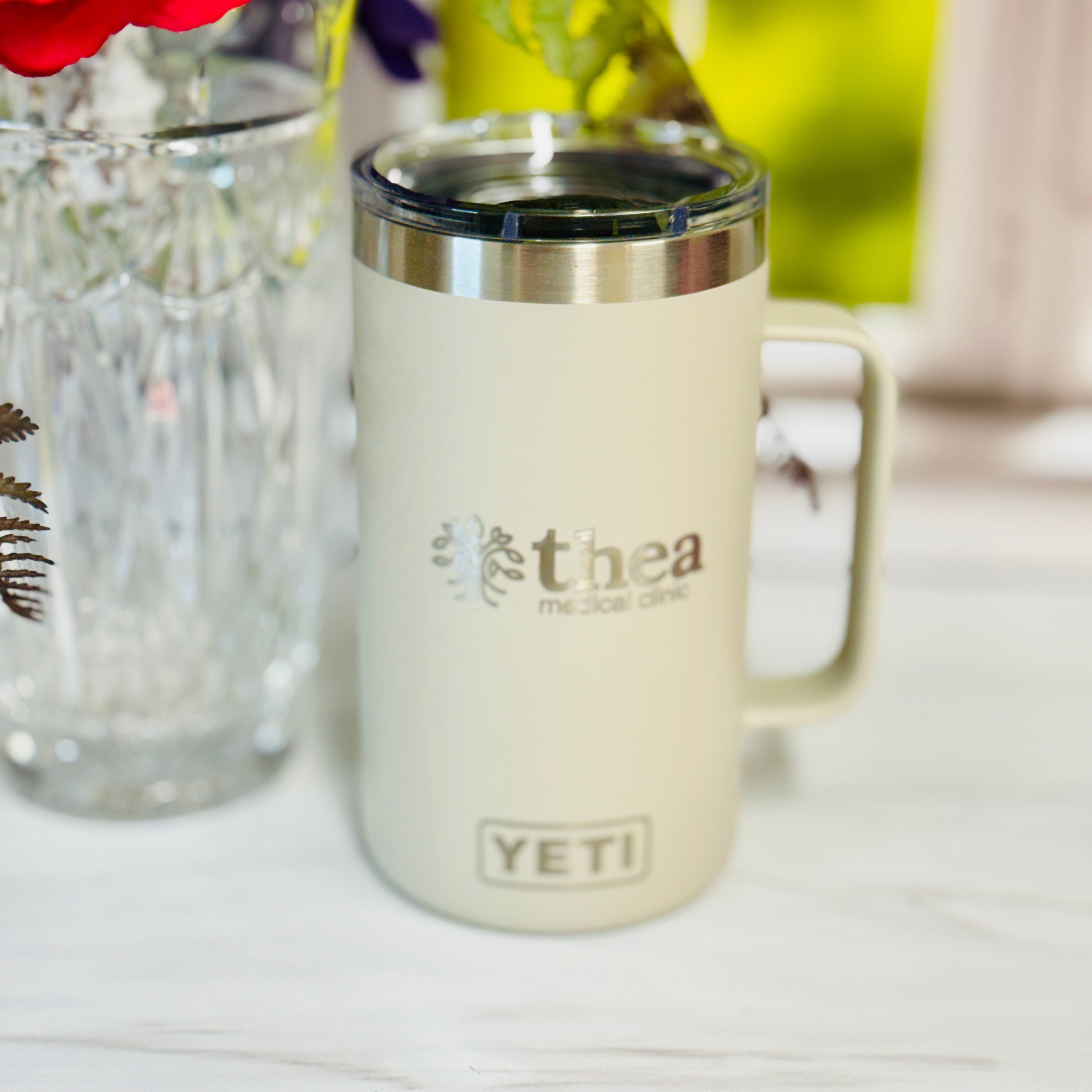 Cream-colored mug with 'YETI' logo on a white surface with flowers in the background