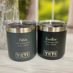 Two YETI tumblers with personalized names and addresses on a wooden surface.