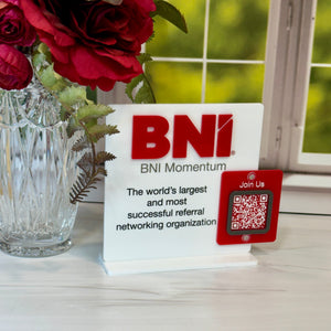 BNI Momentum sign with a QR code on a surface with flowers in the background