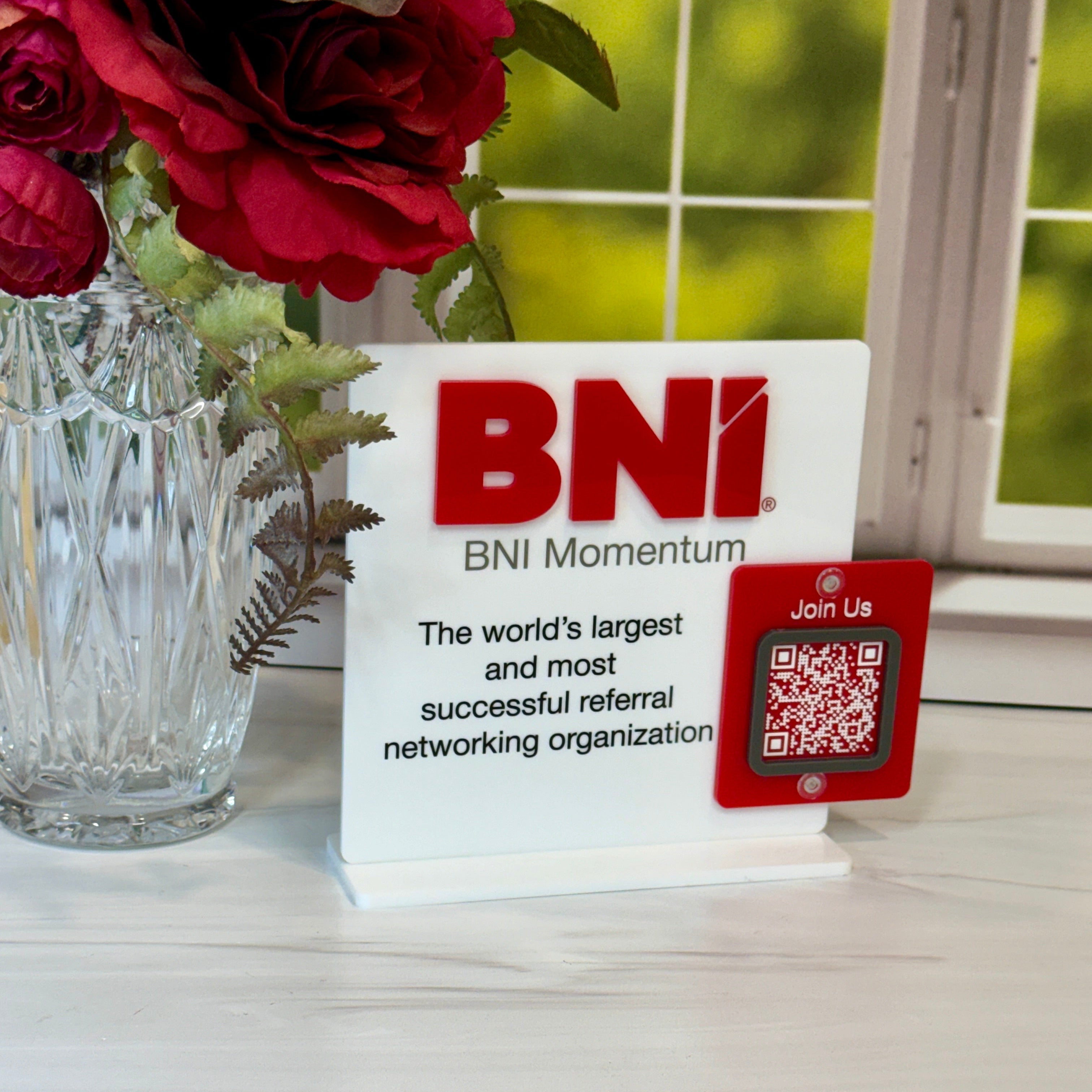BNI Momentum sign with a QR code on a surface with flowers in the background
