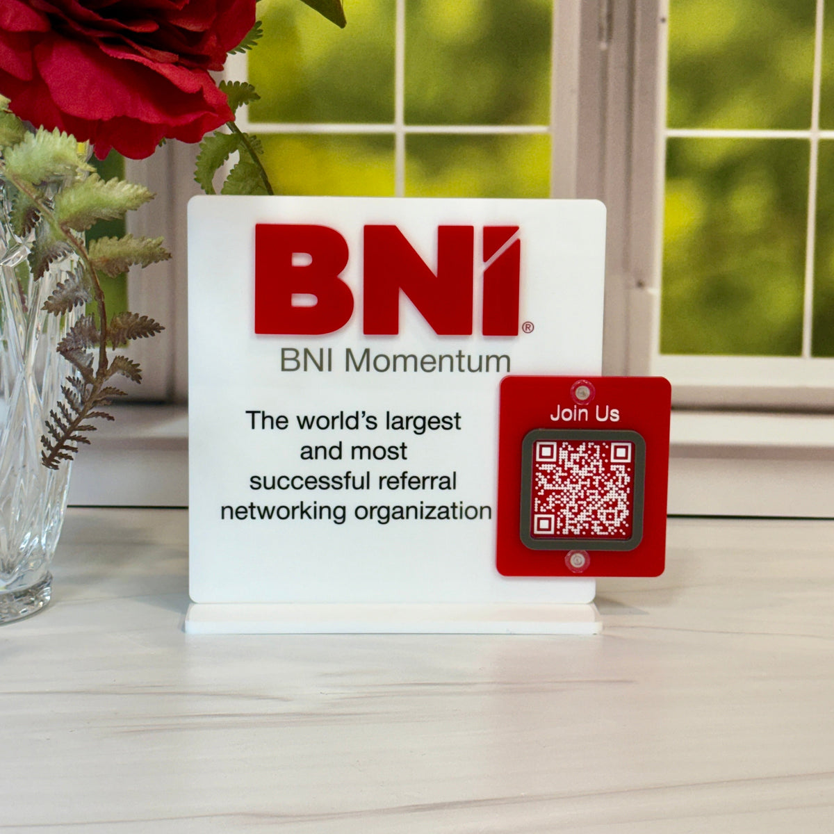BNI Momentum sign with QR code on a table with flowers and window in the background
