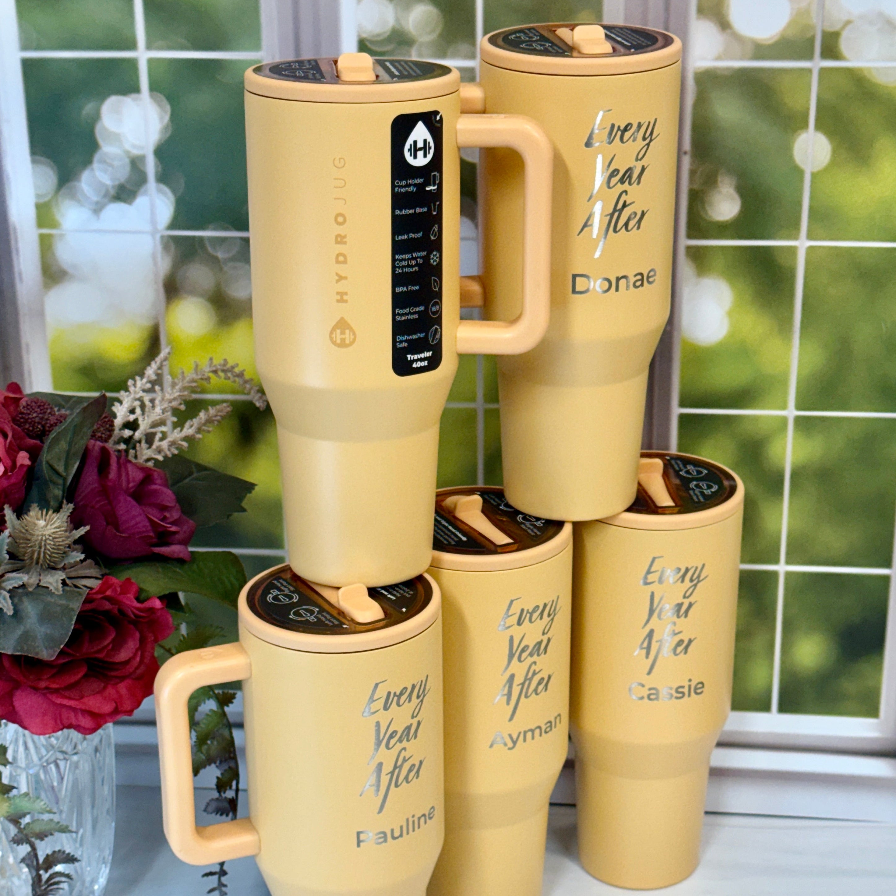 Set of yellow tumblers with personalized names on a windowsill with a blurred outdoor background.