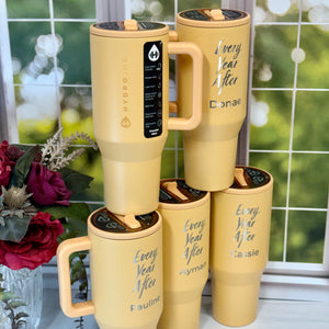 Set of yellow tumblers with personalized names on a windowsill with a blurred outdoor background.