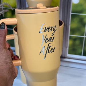 Yellow cylindrical product with 'Every Year After' text held by a hand against a blurred background