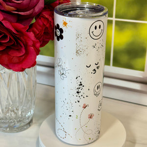 White tumbler with smiley face design next to red roses on a white surface.