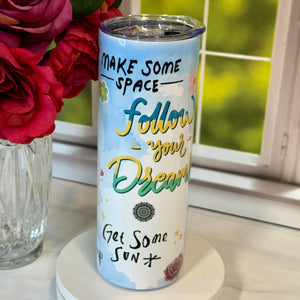 Tumbler with motivational quote on a surface with flowers in the background