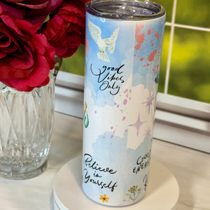 Tumbler with motivational quote and floral design next to red flowers on a light surface.