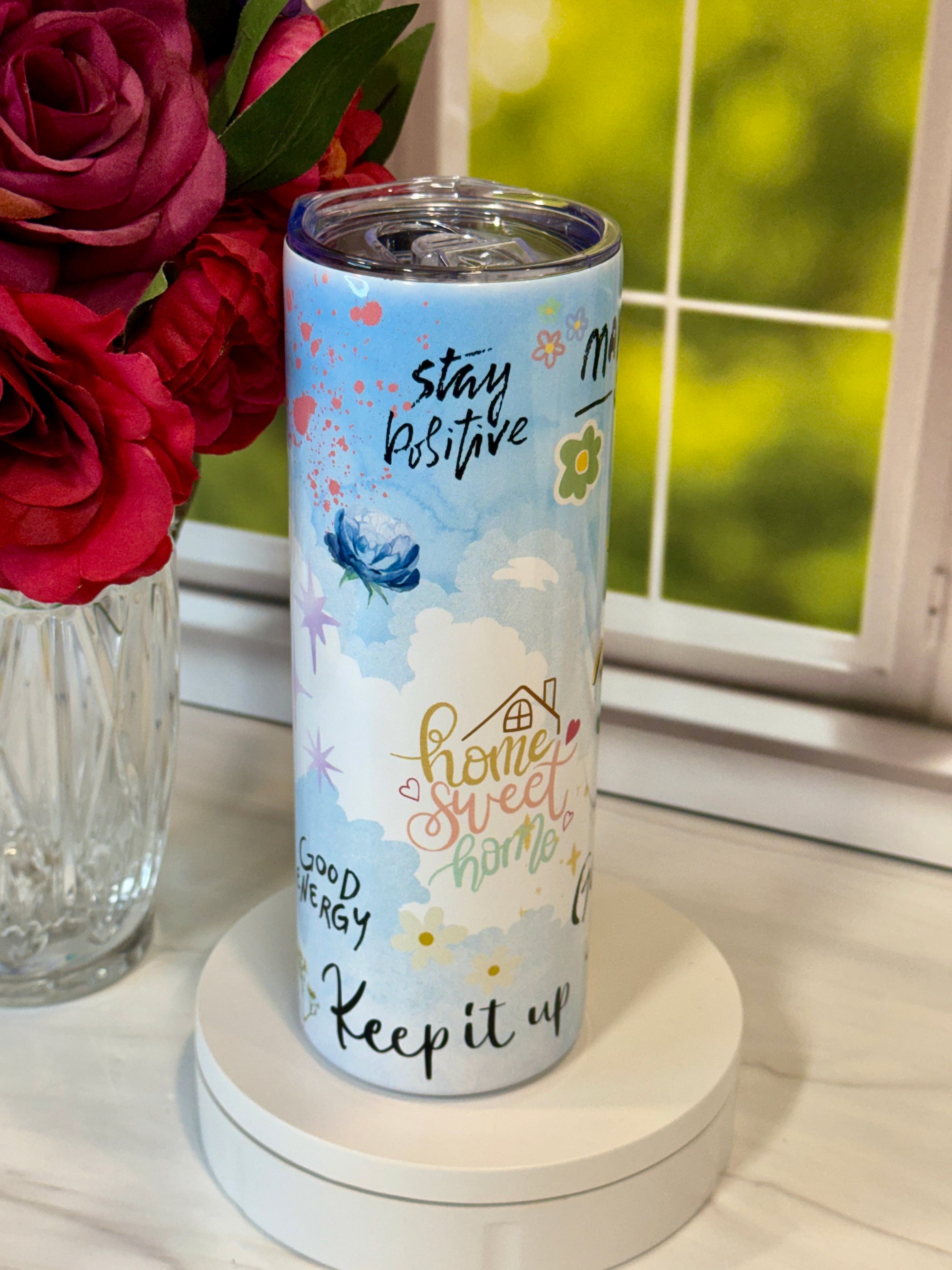 Tumbler with motivational text on a surface with flowers in the background