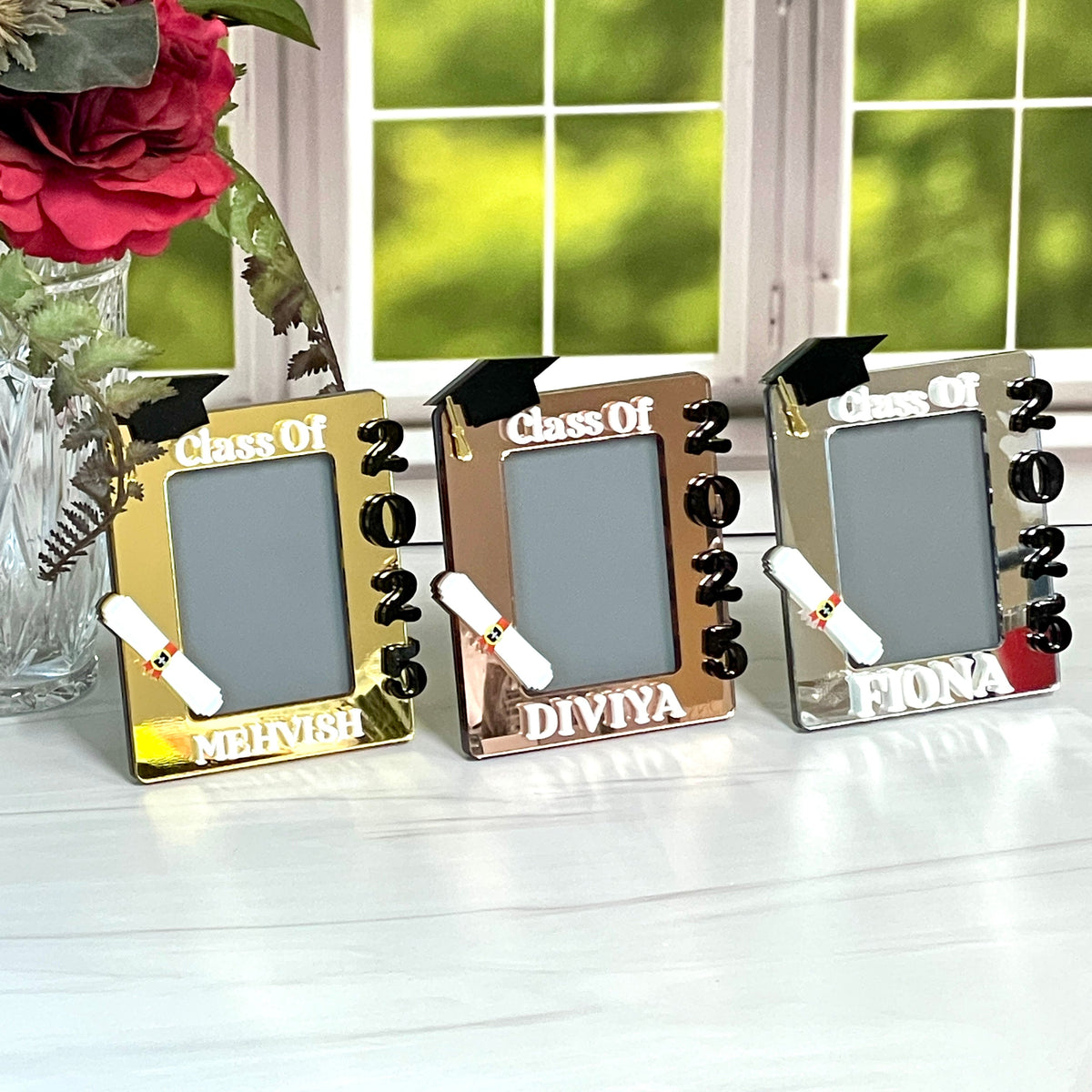 Three graduation-themed photo frames on a surface with flowers in the background.