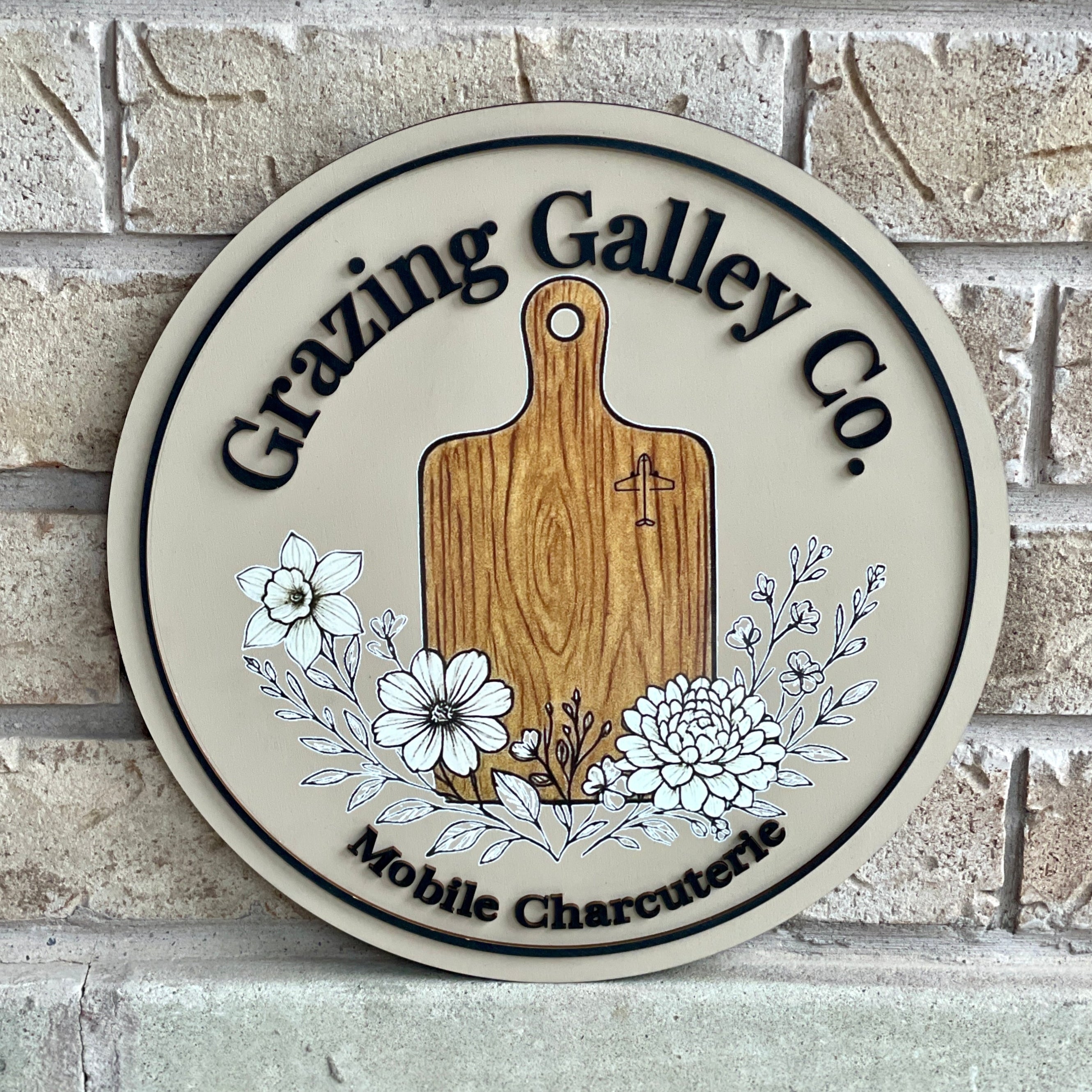 Round wooden sign with 'Grazing Galley Co.' branding on a brick wall background