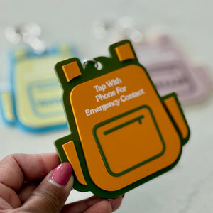 Orange and green emergency contact device held by a hand on a light gray background