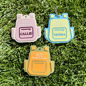 Three backpack-shaped keychains on grass