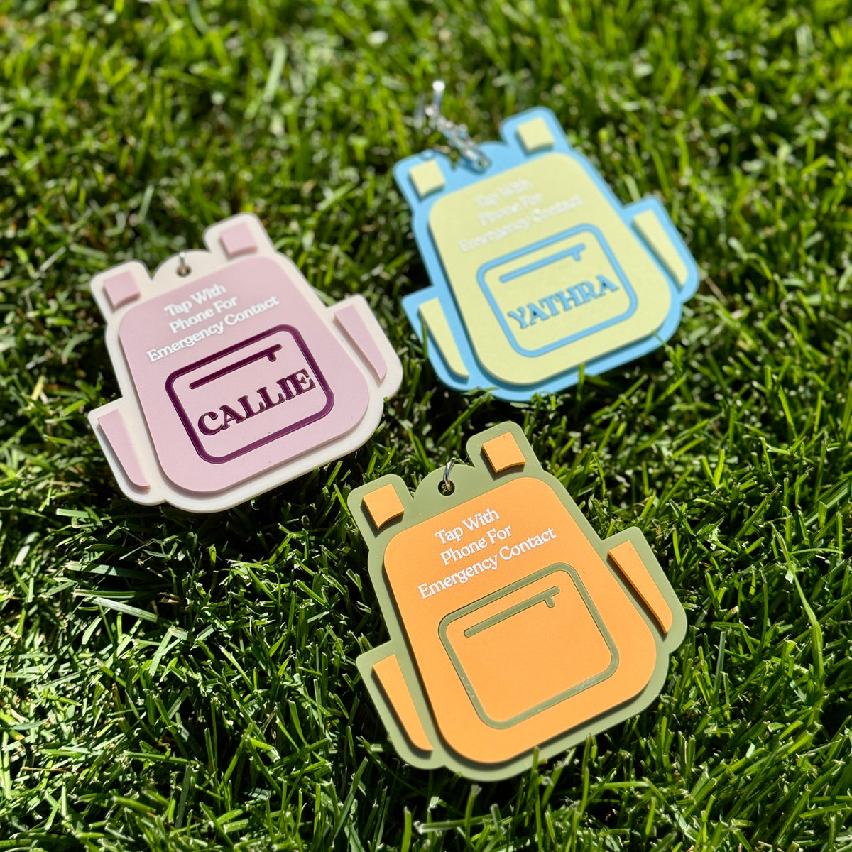 Three colorful backpack-shaped tags on grass