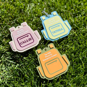 Three colorful backpack-shaped tags on grass